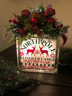 Glowing Reindeer Games light box with a red berry and pine arrangement
