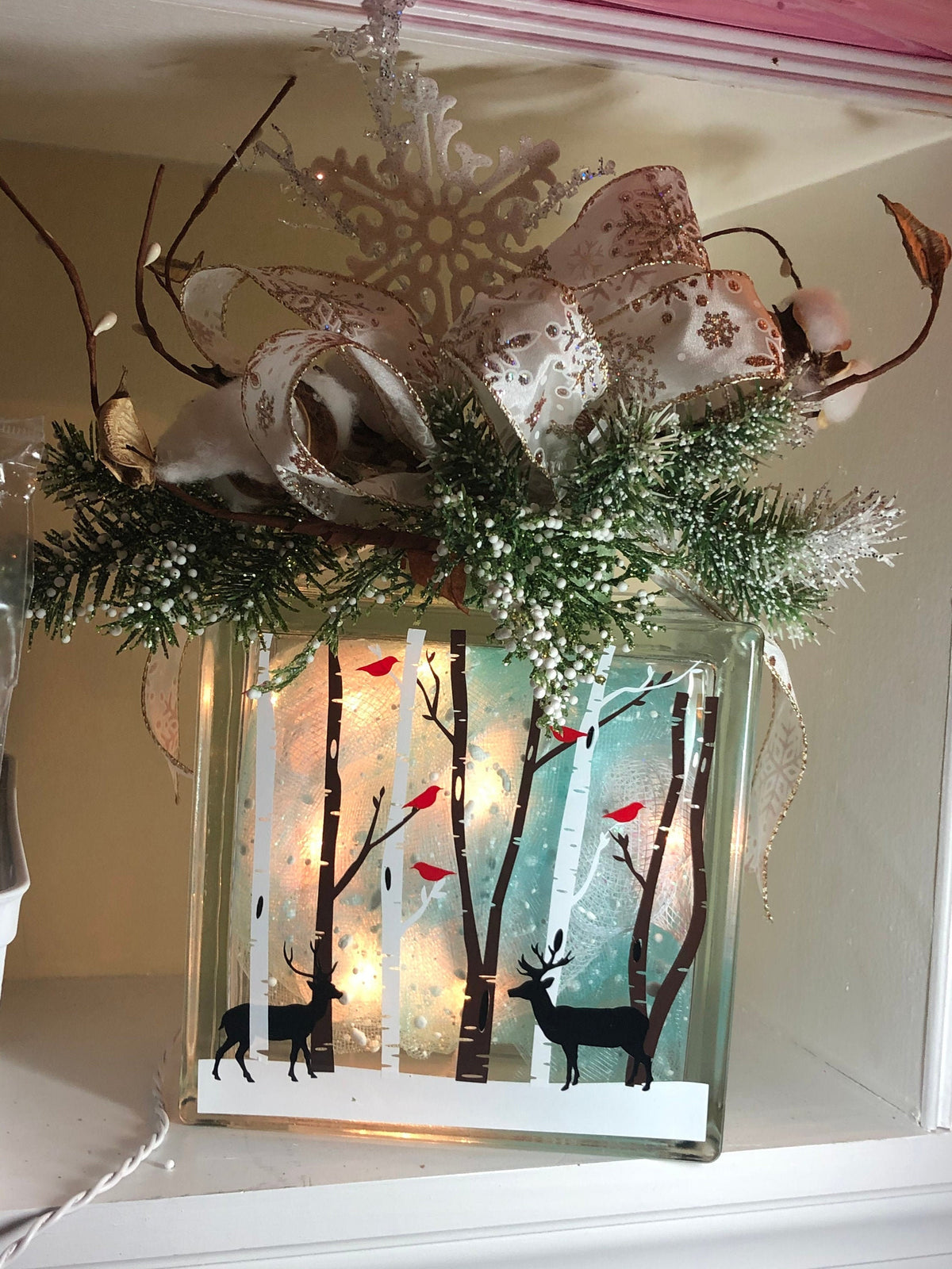A decorative light box with a winter theme, featuring birch trees, deer, and cardinals, encased in a glass box with a decorative bow on top.