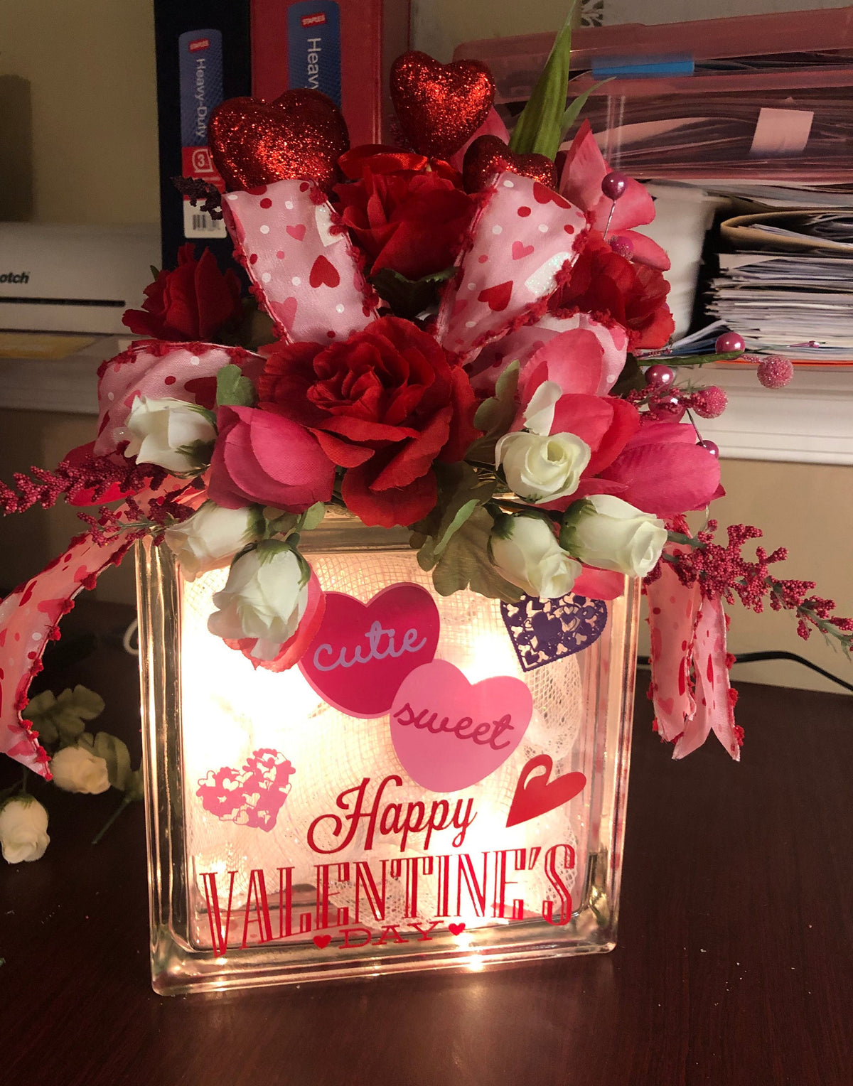 Happy Valentine's light box glowing on a desk, topped with red and pink roses